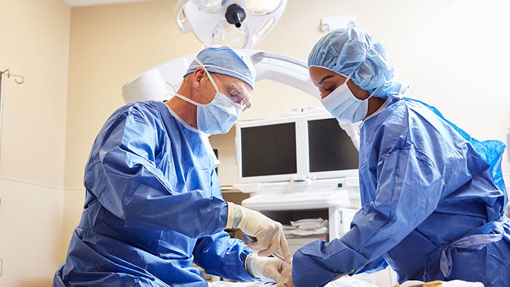 Two surgeons dressed in scrubs operate on a patient.