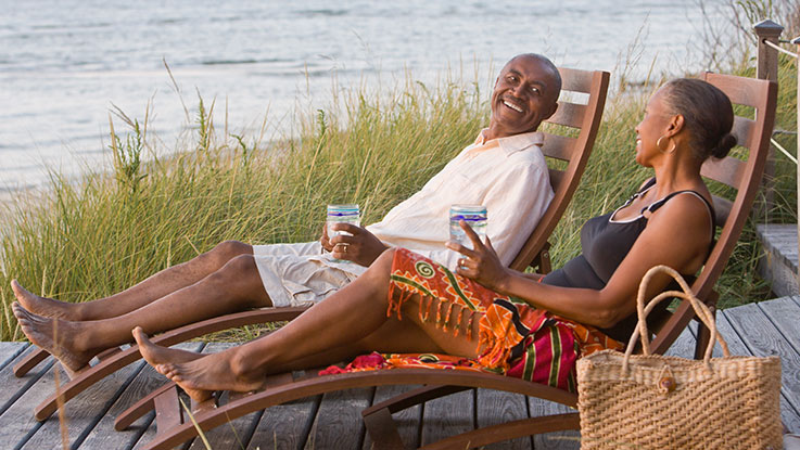 A man and a woman lounge on beach chairs, smiling at each other. 