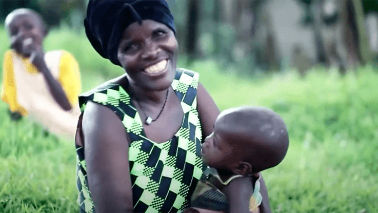 A mother smiles for a picture while holding her baby to her chest.