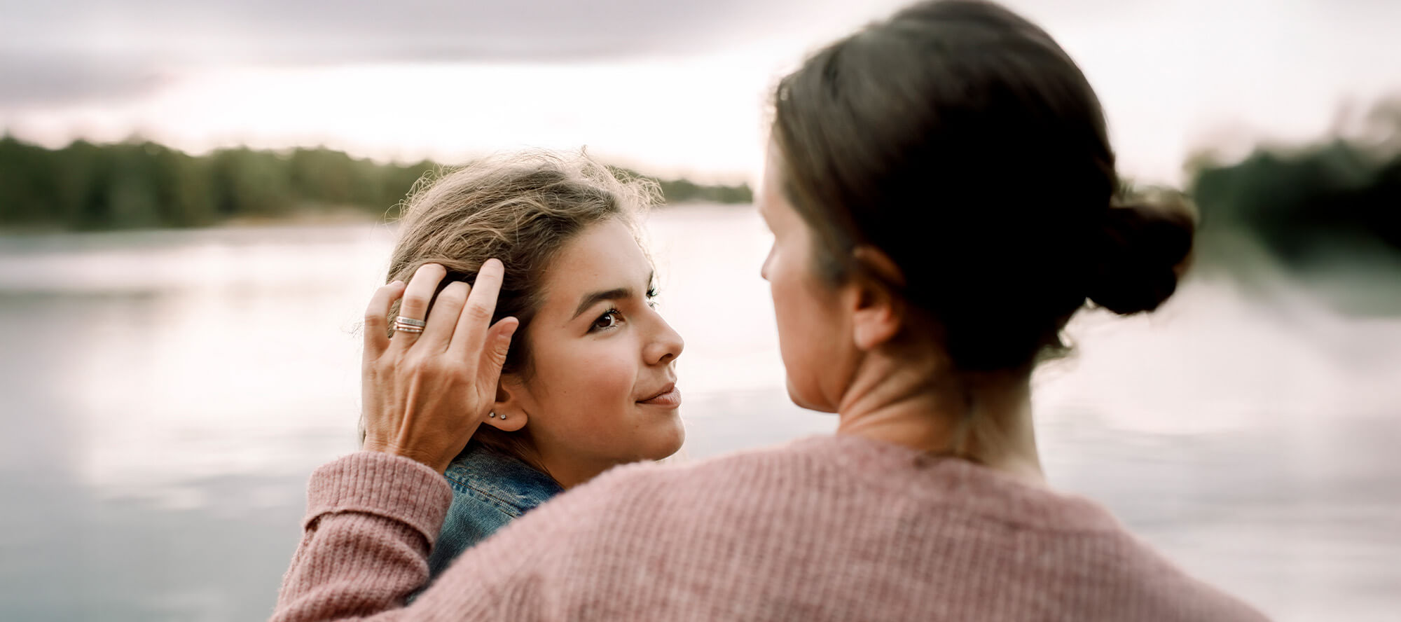 A mom smooths the hair of her tween daughter who is looking up at her with a slight smile.