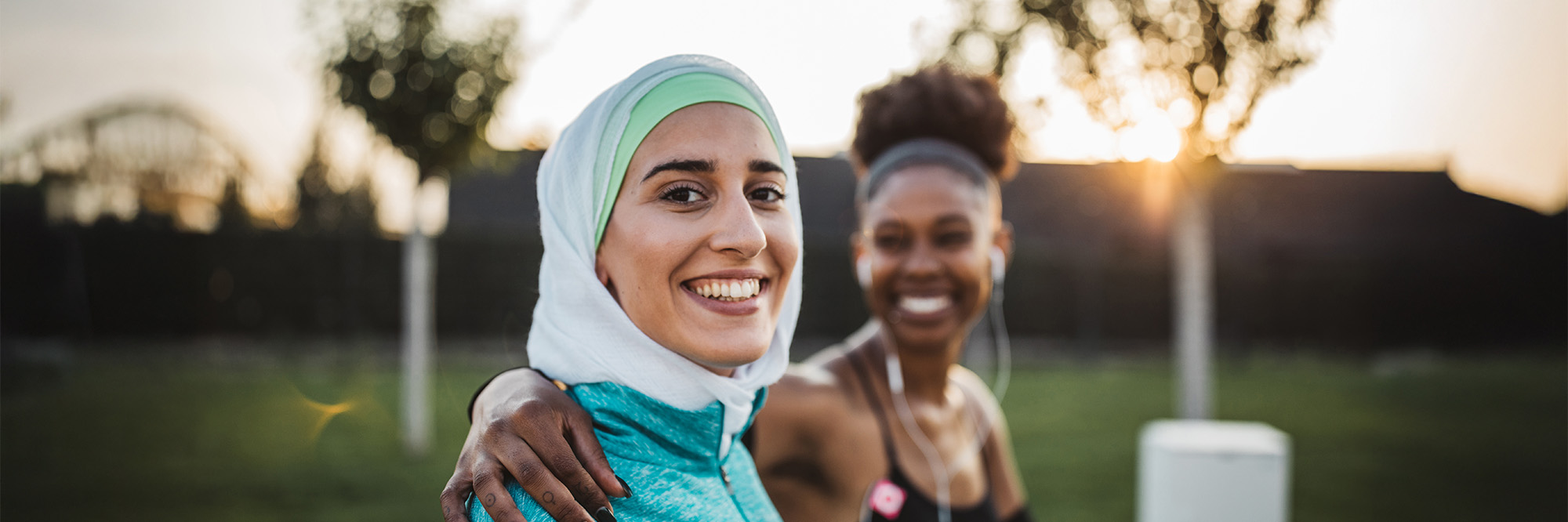 A woman with a head scarf and her female friend smile during an outside walk at dusk.