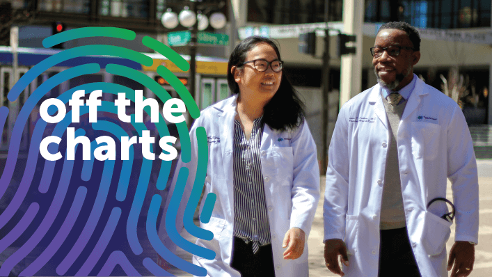 A female Asian doctor and a male Black doctor smile and talk as they walk outside on a sunny day